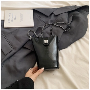 Détail d'un sac seau noir brillant avec serrure argentée et bandoulière chaîne sur lit doux