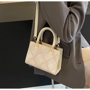 Detail of cream crossbody bag with textured plaid pattern and woven handle on a blazer