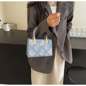Detail of light blue denim handbag with quilted stitching and gold hardware details