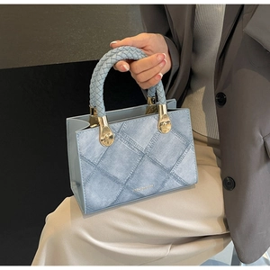 Close-up of a light blue patchwork small square bag with woven handle and gold hardware