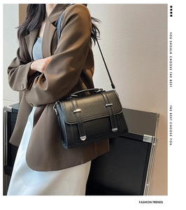 Detail of black pebbled leather crossbody bag with silver buckles on a brown blazer
