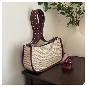 Detail view of woven straw bag with red leather trim and silver metal rivets on strap