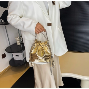 Détail du sac seau doré avec texture crocodile, bandoulière chaîne et longues franges