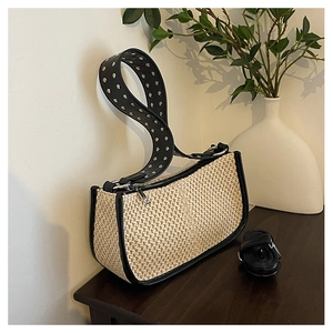 Detail of woven straw shoulder bag featuring silver studded strap and beige raffia texture