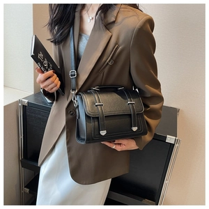 Close-up of a structured black leather crossbody bag with silver buckles on a brown suit