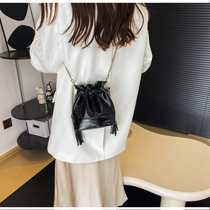 Détail du sac seau noir brillant à cordon avec fine chaîne en métal et pompons