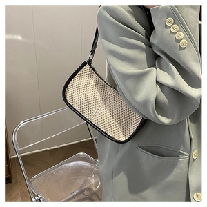Detail of a straw woven shoulder bag with black leather trim worn with a blazer