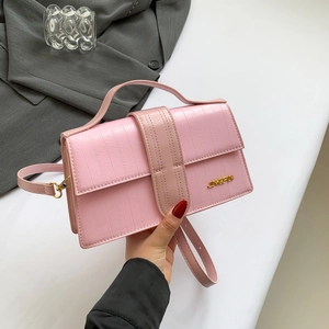 Pale pink crocodile pattern leather handbag with gold logo being held by a model