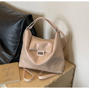 Détail d'un sac beige matelassé avec fermoir rotatif en métal argenté sur socle