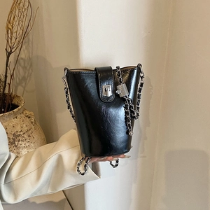 Borsa a secchiello nera lucida con catena d'argento e chiusura in un ambiente minimalista