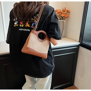 Détail du sac seau en paille tissée avec contraste en cuir marron et bandoulière chaîne