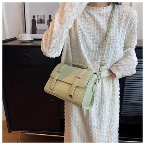 Detail of a sage green leather crossbody bag with metal buckles and adjustable strap