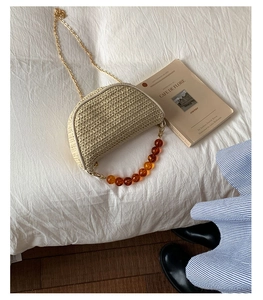 Detailed macro of a woven straw mini crossbody bag with amber beaded handle and gold chain