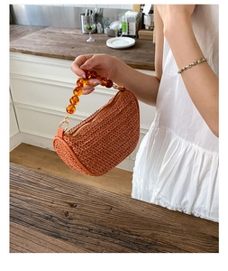 Detail of terracotta straw bag with luxury amber bead handle and gold zipper closure