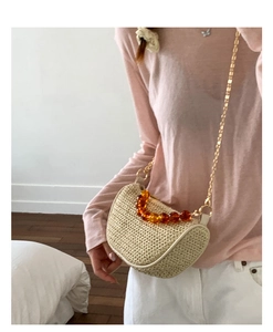 Detail of straw woven saddle bag with amber bead handle and gold metal chain strap
