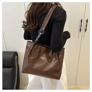 Rear view of brown patchwork tote bag with gold chain strap on model's shoulder