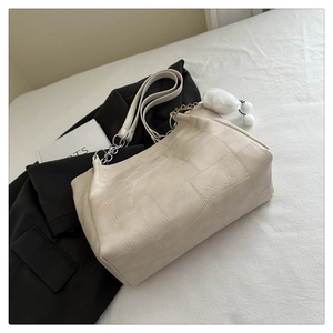 Detail of cream tote bag with geometric stitching and a white plush pom-pom charm