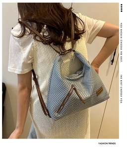 Detail of blue and white herringbone straw tote bag with brown leather straps and zip pocket