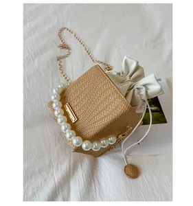Detail of straw crossbody bag featuring pearl handle, metal chain and drawstring lining