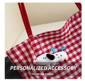 Detail of red checkered canvas tote bag with a cute plush dog charm on a white background