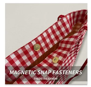 Close-up of golden magnetic metal snap buttons on a red and white plaid nylon tote bag