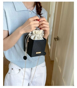 Detail of black woven handbag featuring pearl top handle and gold chain shoulder strap