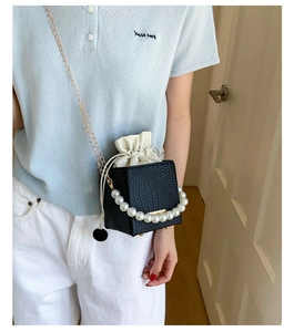 Crossbody view of a black woven mini bag with large pearl handle and gold chain strap
