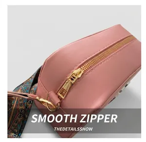 Detail of pink leather bag featuring a smooth gold zipper and colorful woven strap