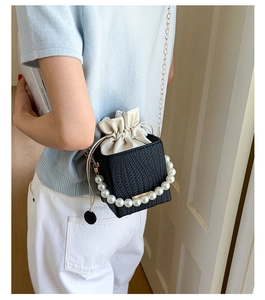 Chic black woven bucket bag with pearl handle and gold chain worn by a model