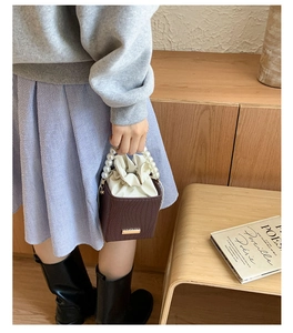 Detail of brown bucket bag with pearl handle and white drawstring liner in a retro scene