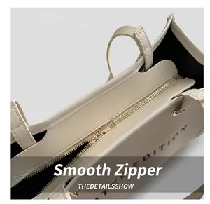 Detail view of smooth golden metal zipper closure and black lining on off-white tote bag