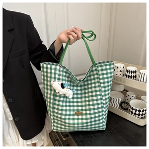Detail of green plaid canvas tote bag with cute plush puppy charm and handmade metal label