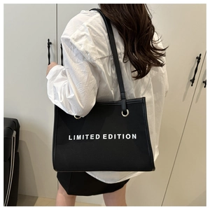 Detailed view of black canvas tote bag with white LIMITED EDITION print on model