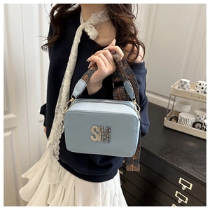 Close-up of light blue crossbody bag with metallic SM logo and bohemian jacquard strap