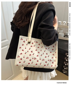 Close-up of white tote bag with red cherry print worn by a model in a cozy office setting