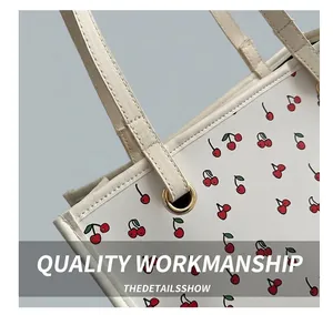 Detail of white tote bag featuring red cherry prints and reinforced golden eyelets