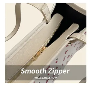 Détail de la fermeture éclair dorée sur sac crème avec imprimé cerise et texture cuir