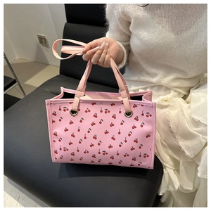 Détail d'un sac cabas en toile rose avec motif cerises et poignées en cuir pour femme