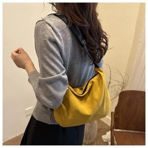 Detail view of large yellow dumpling crossbody bag with adjustable black strap worn by model