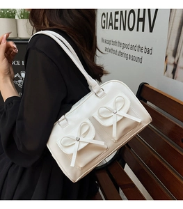Detail of white faux leather shoulder bag featuring decorative bows and double pockets