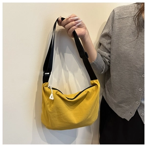 Detail of a bright yellow canvas crescent bag with a black zipper and adjustable strap