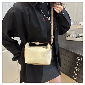 Detail of cream-colored pleated crossbody bag with brown leather trim and metal zipper