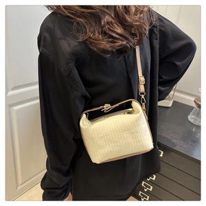 Close-up of cream-colored pleated crossbody bag with brown leather trim and gold buckle