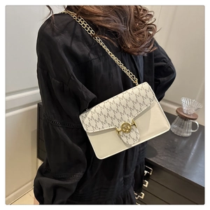 Close-up of contrast color handbag featuring M-pattern texture and gold chain strap