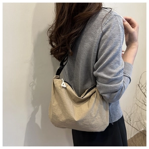 Side view of light khaki crossbody bag with adjustable strap and triangular zipper pull