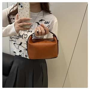 Detail showing brown pleated texture and zipper closure on a stylish women's satchel bag