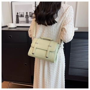 Detail of sage green crossbody bag with silver buckles worn over a white dress