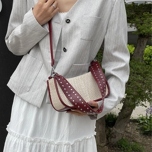 Straw hobo bag with burgundy leather strap and metallic rivets on a model in a garden