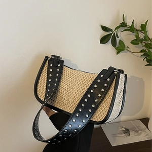 Chic beige straw baguette bag with black leather trim and silver studs in lifestyle setting