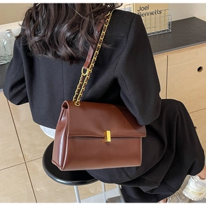 Close-up of caramel leather tote bag with gold buckle and chain strap on a wooden stool